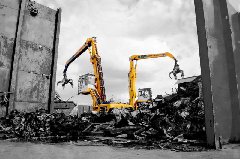 Yellow ASM grabbing machines working in a scrap metal yard